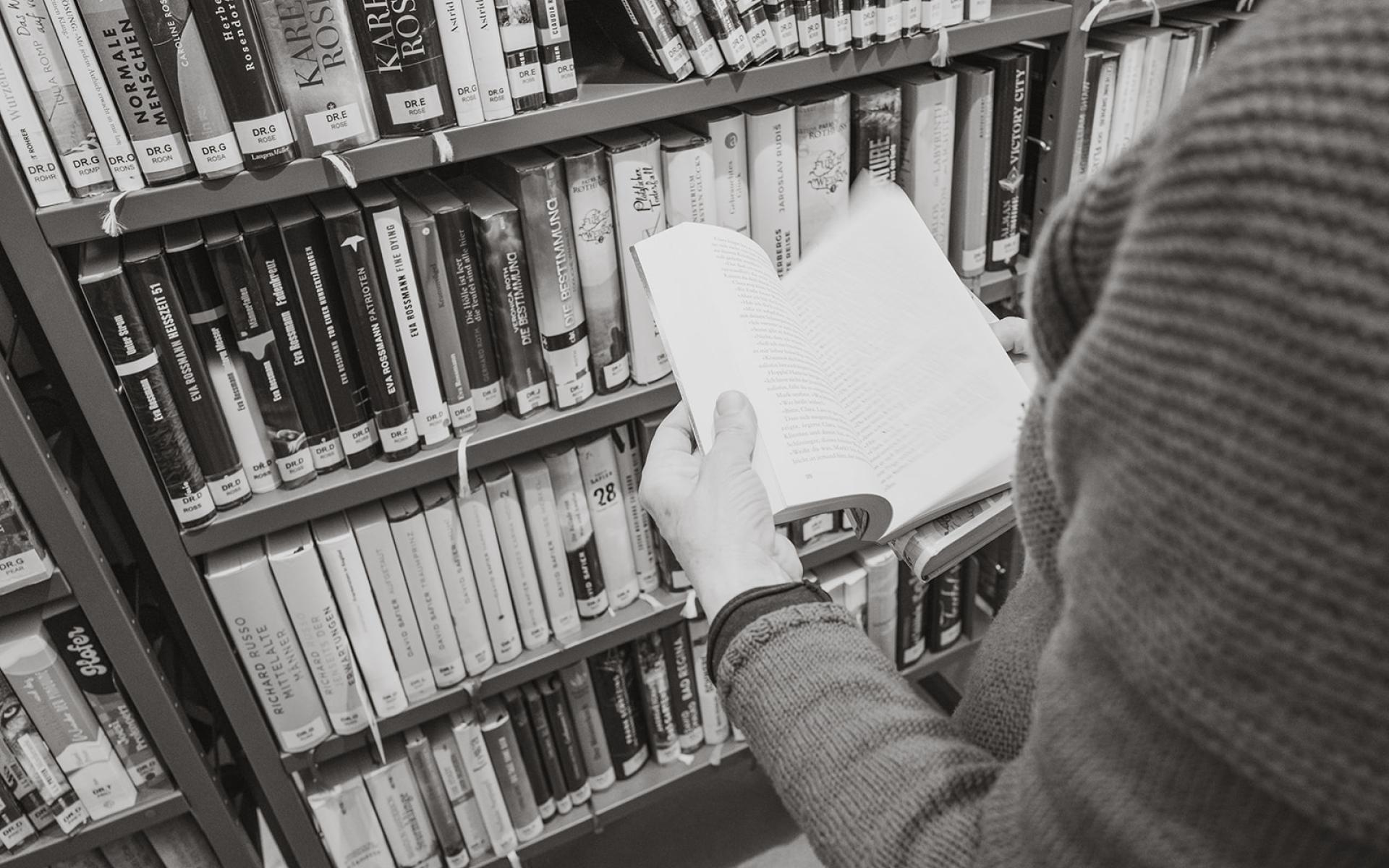 in Buch plätternde Person vor Bücherregal